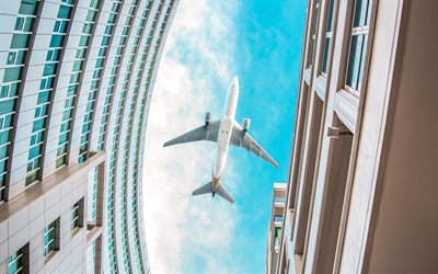 passenger plane over buildings, plane over the city, airplane bottom view, blue sky, building, air travel concept