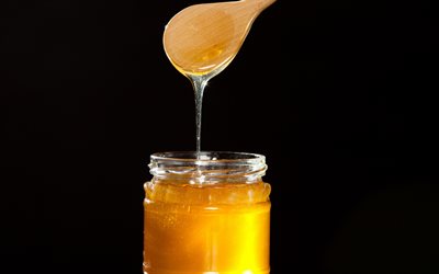 honung, sked med honung, honung burk p&#229; svart bakgrund, honung burk, honung begrepp