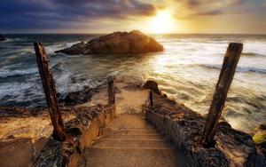 A beautiful sunset, with a set of stairs leading down to the water. 1440p wallpaper