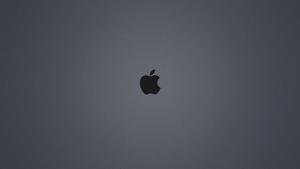 A dark-gray background illuminated by the iconic black Apple logo Wallpaper