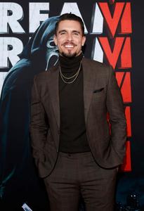 a man in a suit and a turtleneck standing in front of a poster scream wallpaper