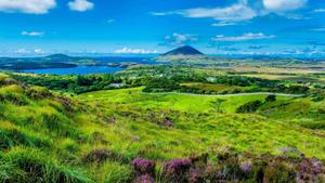 a view of a green hill with a lake and mountains Wallpaper