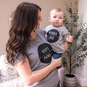 a woman holding a baby wearing a grey shirt that says dotty dotty mama matching wallpaper
