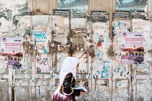 a woman walking past a wall with posters palestine wallpaper