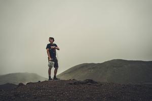 Man In Black T-shirt And Brown Shorts Standing On Brown Rock meme wallpaper