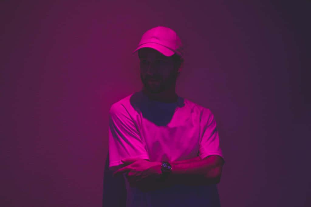 a man in a hat and a cap standing in front of a purple wall — 1024x683 wallpaper