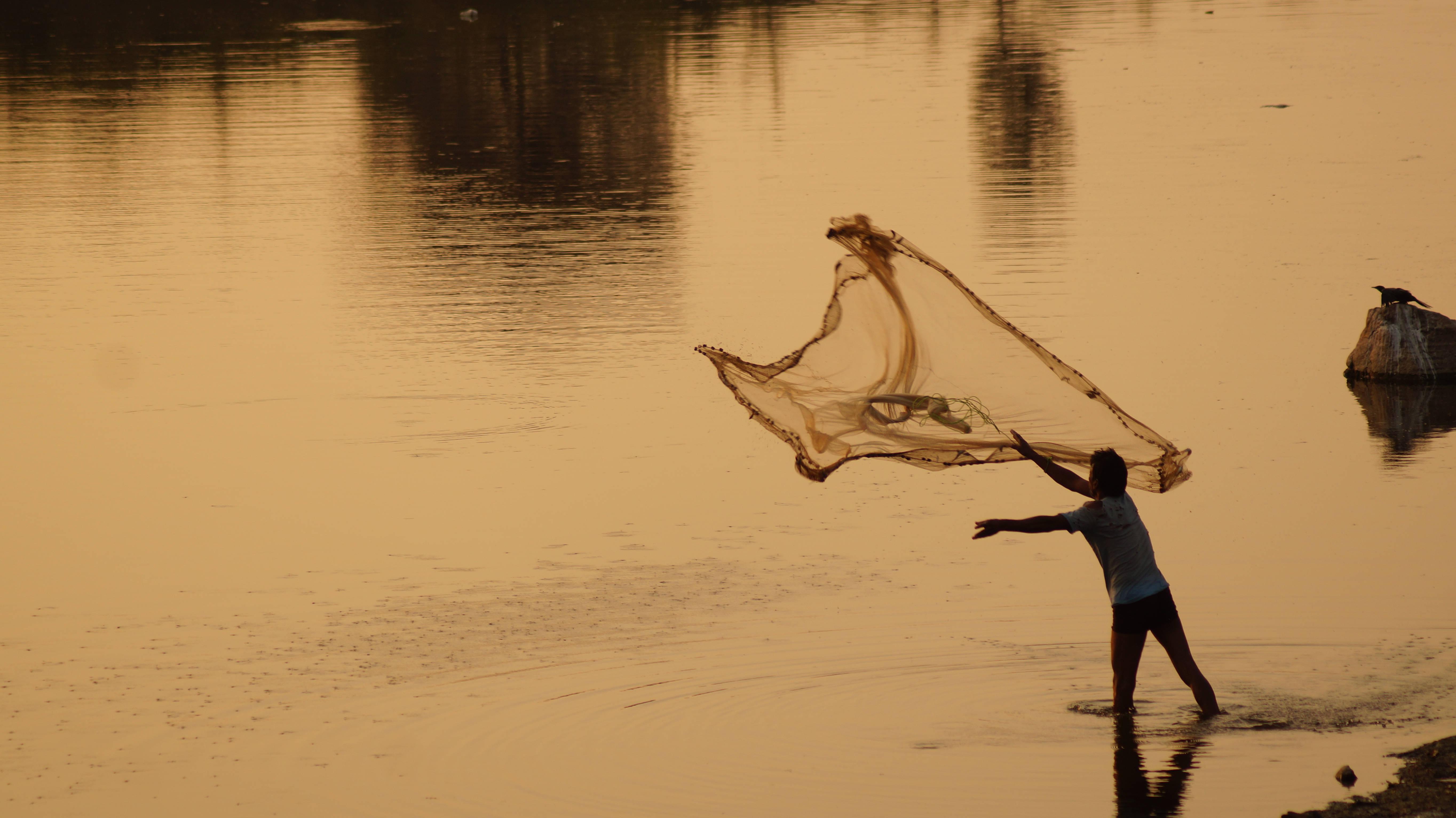 A man spreads a fishing net to haul in the morning's catch. — 5456x3064 wallpaper