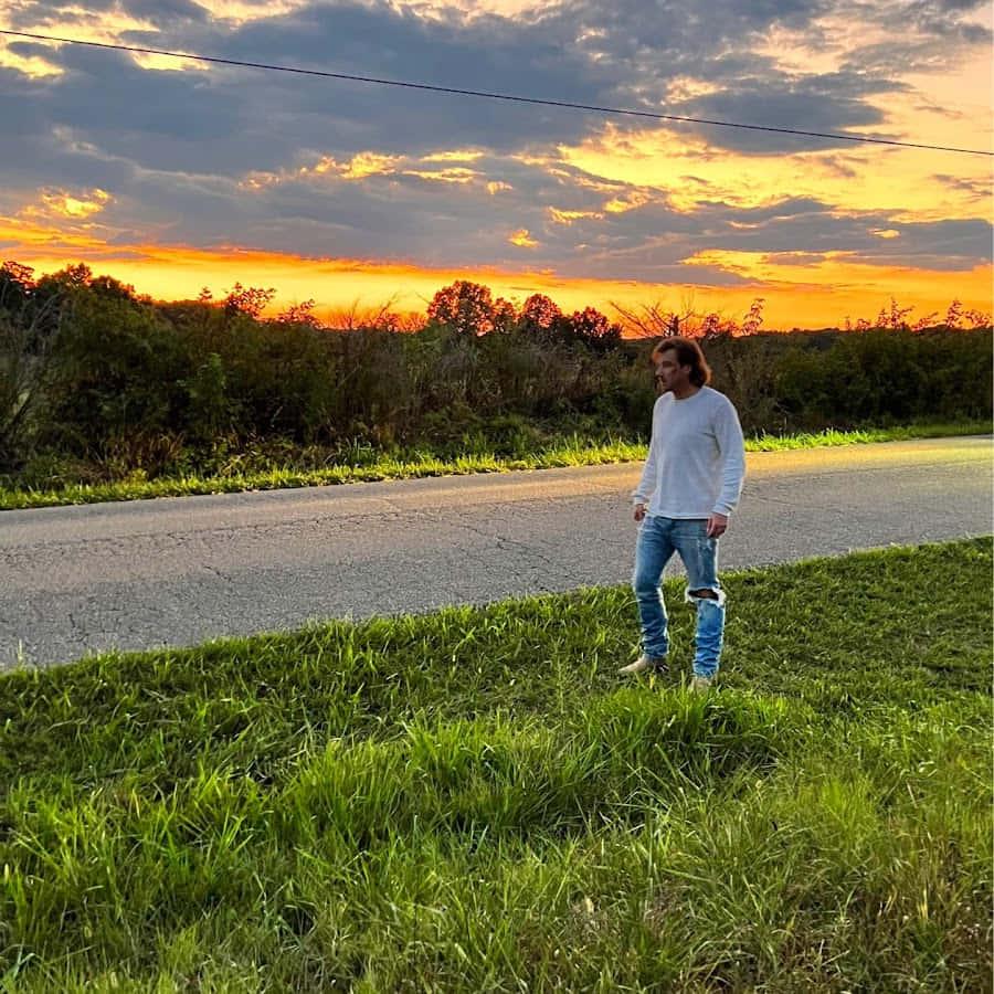 a man standing on the side of a road at sunset — 900x900 wallpaper