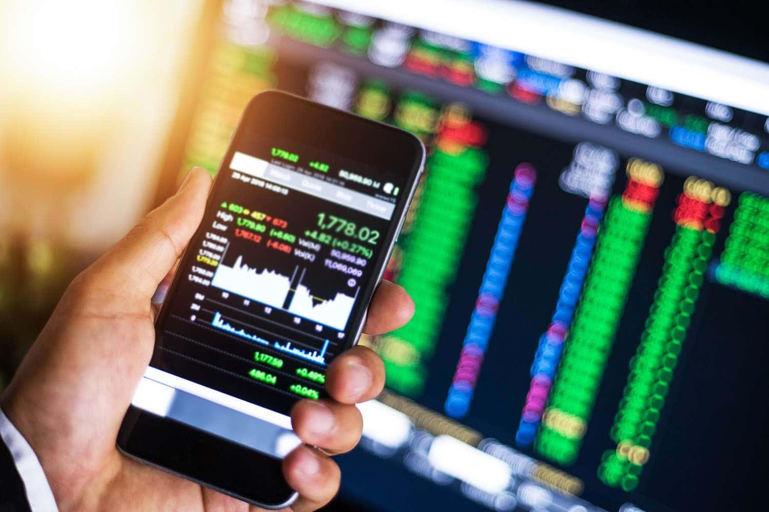 a person holding a smartphone with stock market data on it — 1500x1000 wallpaper