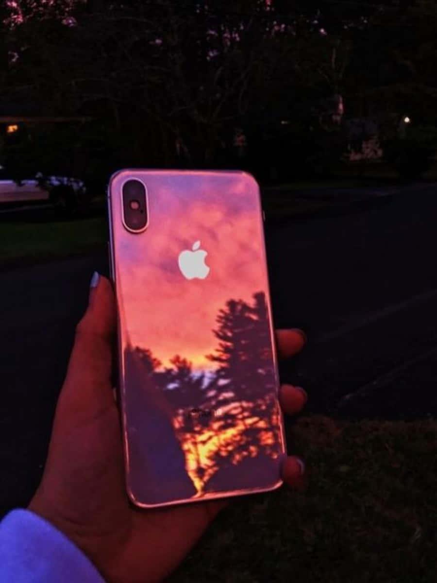 a person holding an iphone with a sunset reflected in it