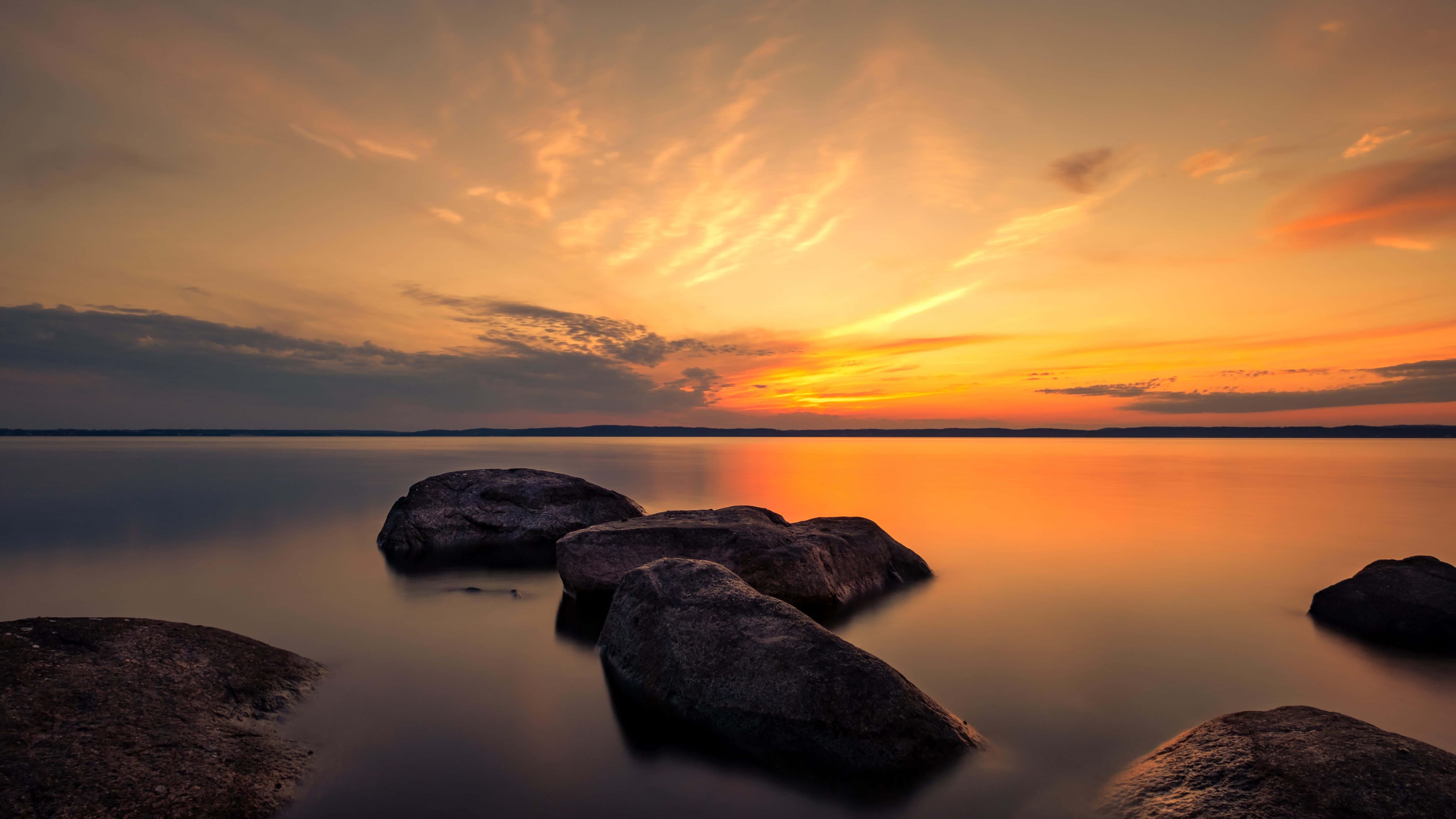 a sunset with rocks and water in the background — 5991x3370 wallpaper