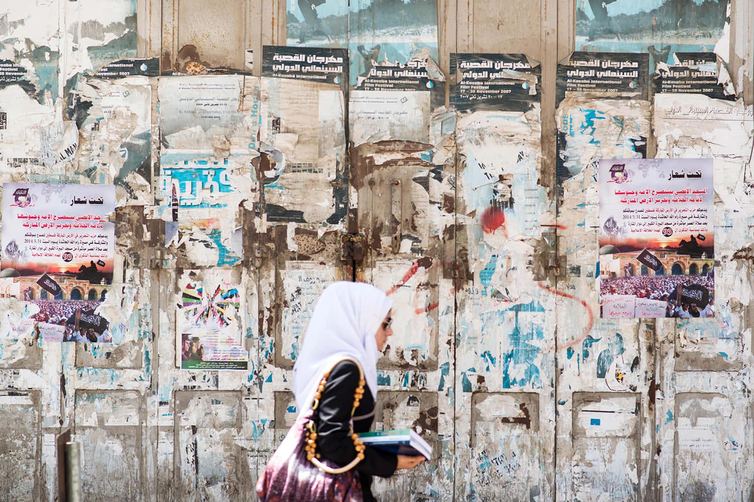 a woman walking past a wall with posters — 1500x1000 wallpaper